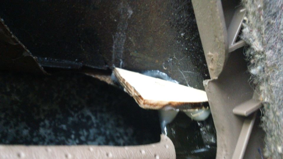 Close-up of a damaged car interior panel with a piece of wood wedged in it