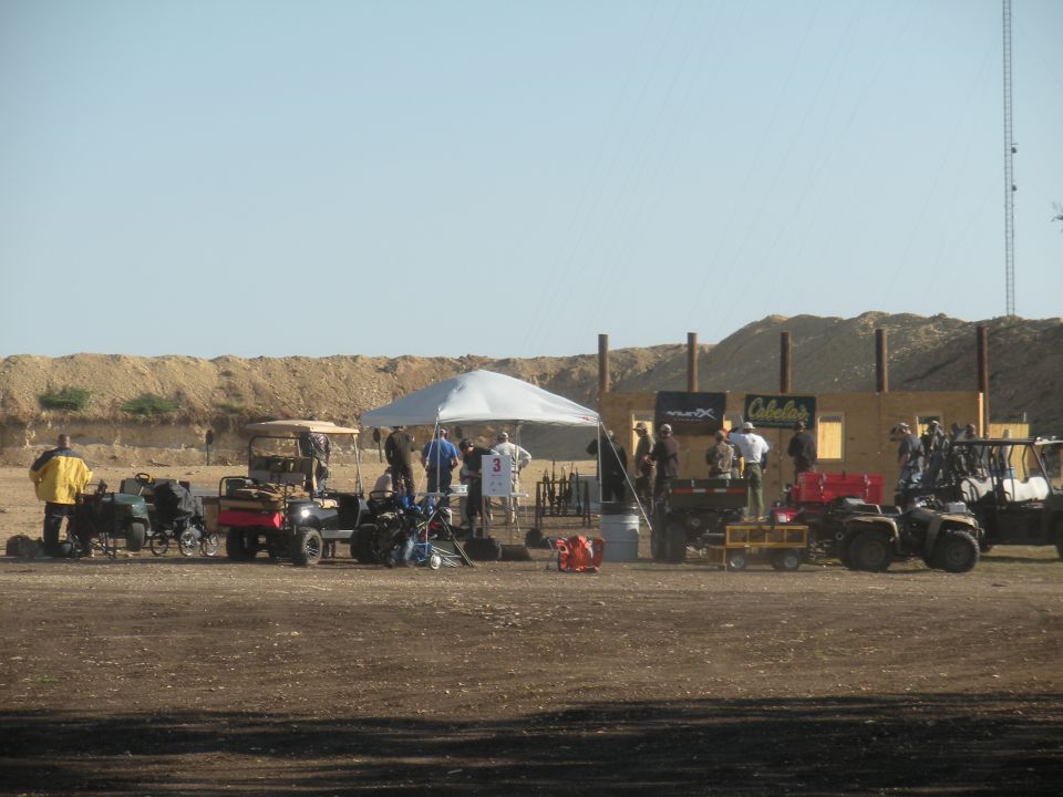Outdoor shooting range setup with ATVs, tents, and people gathered