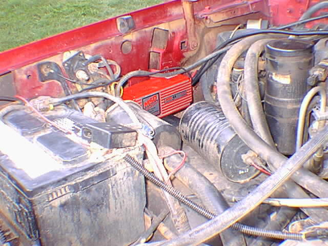 Engine bay of red Bronco with red MSD ignition box, battery, hoses and wiring visible
