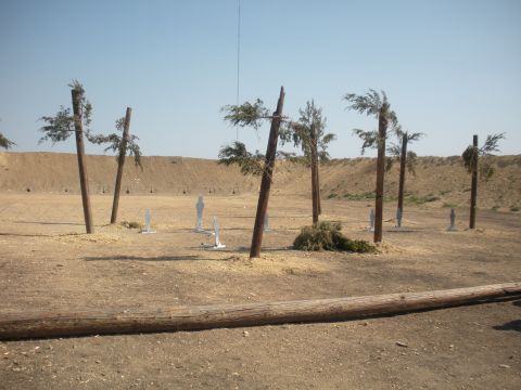 1996 Ford Bronco - A desert shooting range is set up with target silhouettes and artificial trees, under a bright, clear sky.