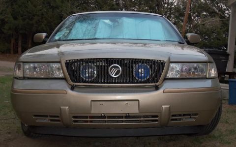 2000 Mercury Grand Marquis - The front grille of a gold Mercury Grand Marquis is visible, with blue lights inside the headlights.
