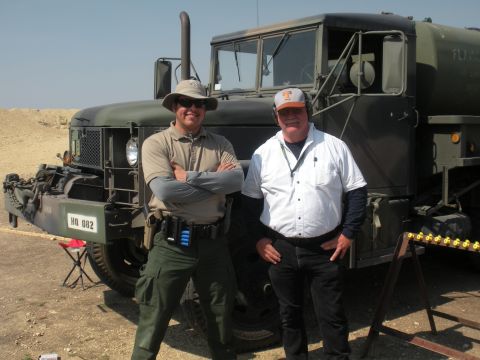 1996 Ford Bronco - Two men pose for a photo in front of a large military truck on a sunny day.