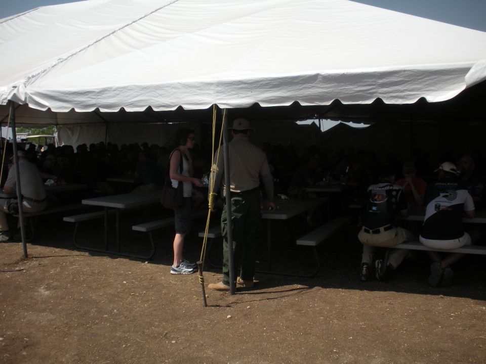 People gathered under a large white tent at picnic tables