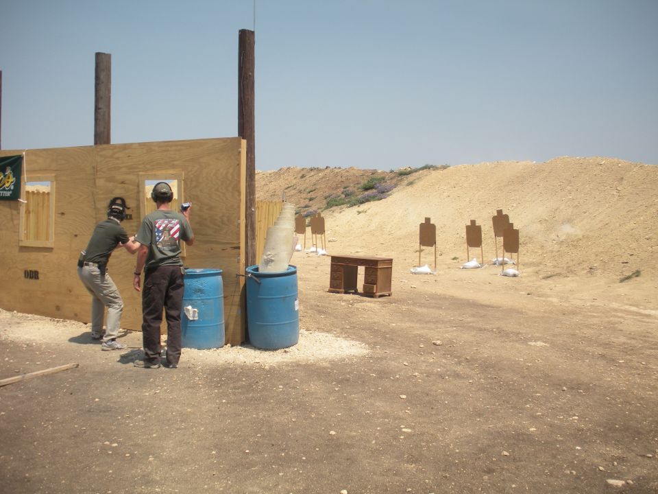 Two people at a shooting range with targets and barrels