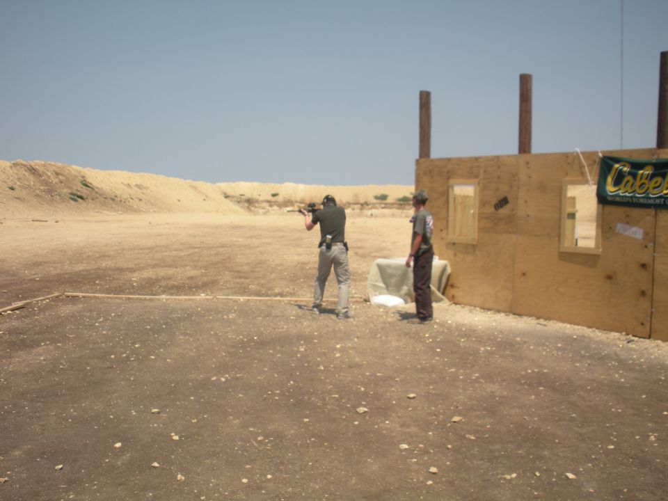 man shooting rifle at outdoor range, another man watching