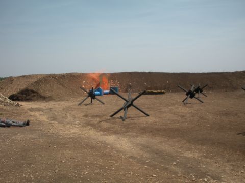 1996 Ford Bronco - A dummy lies on the ground at a target range, with anti-tank obstacles and a target in the background.