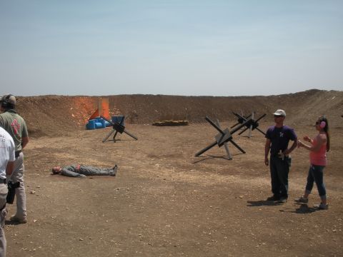 1996 Ford Bronco - A shooting range scene with targets, obstacles, and people observing a dummy lying on the ground.