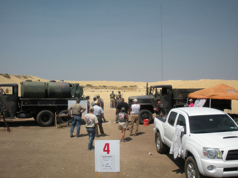 White pickup truck parked next to military trucks at a desert range