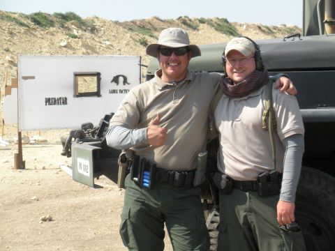 1996 Ford Bronco - Two men stand together at a shooting range with a target and a large vehicle in the background.