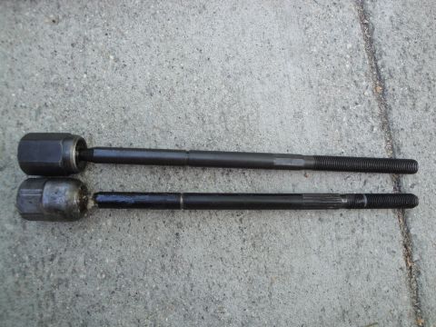 2003 Ford Taurus - Two automotive tie rod ends are shown side-by-side on a concrete surface.