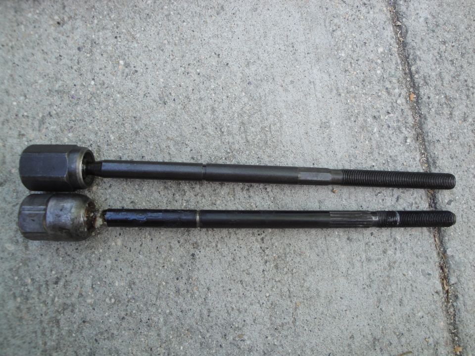Two tie rod ends, one with a hexagonal joint and the other with a rounded joint, laid on concrete