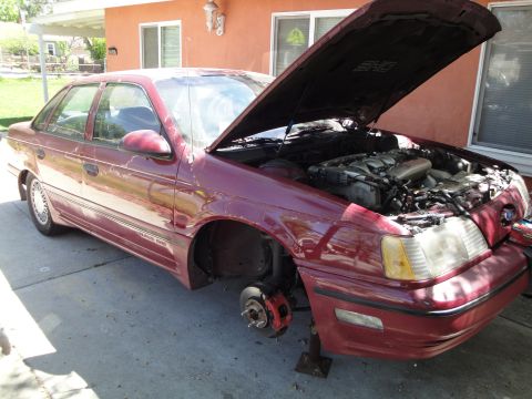 2003 Ford Taurus - This maroon sedan, identified by its "Taurus SHO" badging, is missing a front wheel and has its hood open, exposing the engine.