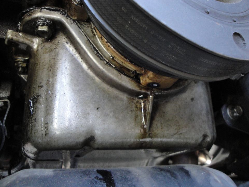 Engine oil pan showing a leak and oil residue. A pulley or brake rotor is visible above