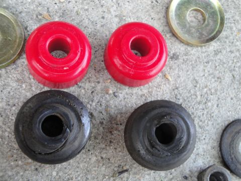 2003 Ford Taurus - Comparison of new red polyurethane and old black rubber suspension bushings laid out on a concrete surface.