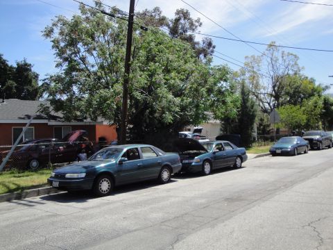 2003 Ford Taurus - A line of sedans are parked along the street, with one green sedan prominently in the foreground.
