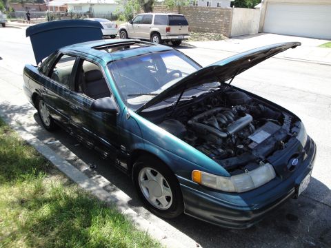 2003 Ford Taurus - A green sedan with its hood and trunk open is parked on the side of a residential street.