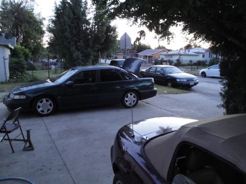 2003 Ford Taurus - A dark green sedan with its trunk open is parked on a concrete driveway, alongside other vehicles.