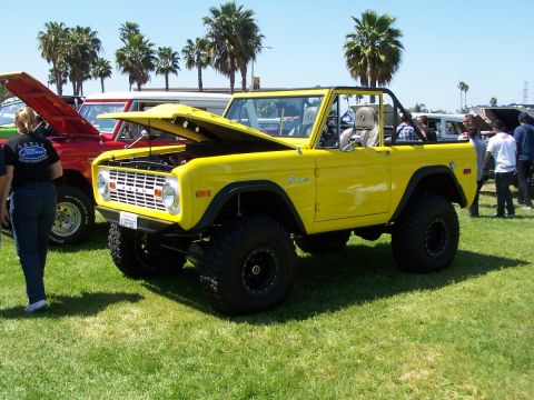 1990 Ford Bronco - A bright yellow Ford Bronco is on display at an outdoor event, with its hood open.