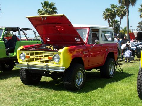 1990 Ford Bronco - A classic red and yellow Ford Bronco is displayed with its hood up at an outdoor event.