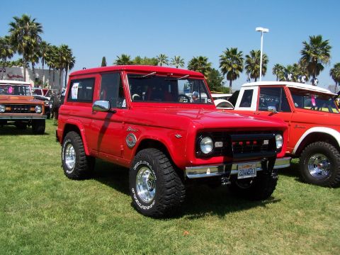 1990 Ford Bronco - A classic red Ford Bronco is displayed outdoors on a sunny day, with other vehicles visible in the background.