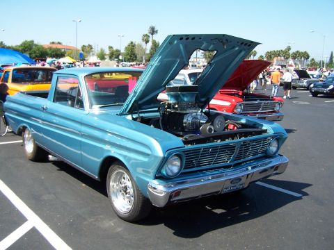 1990 Ford Bronco - A blue 1964 Ford Falcon Ranchero is displayed with its hood open, revealing a supercharged engine, at an outdoor car show.