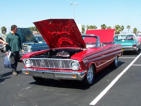 1990 Ford Bronco - A classic red convertible is displayed with its hood open at an outdoor car show.