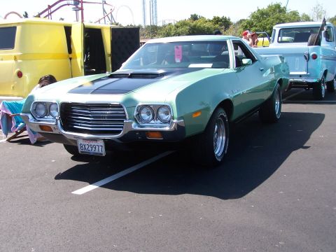1990 Ford Bronco - Three-quarter front view of a light green early-1970s Ford Ranchero coupe utility at an outdoor car show, with a matte-black hood stripe an…
