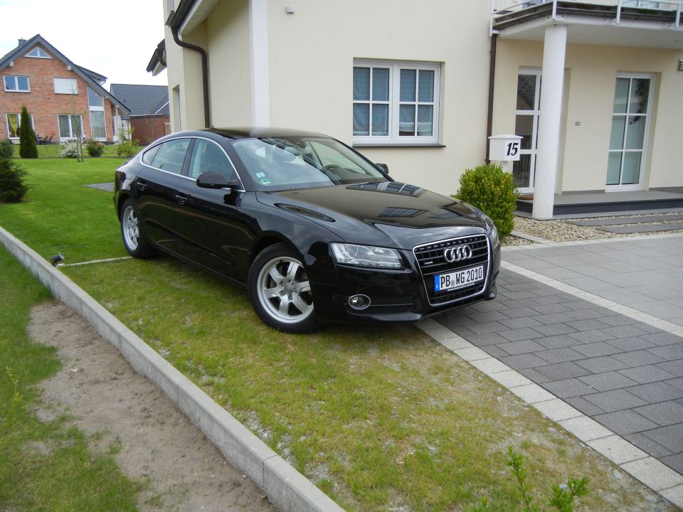 Black 2010 Audi A4 parked on grass in front of a modern house