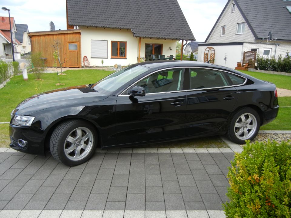 Black Audi sedan parked in driveway. The car is a four-door model with a sloping roofline