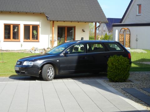 2003 Audi A6 - A dark sedan is parked in a driveway next to a house and a manicured bush.