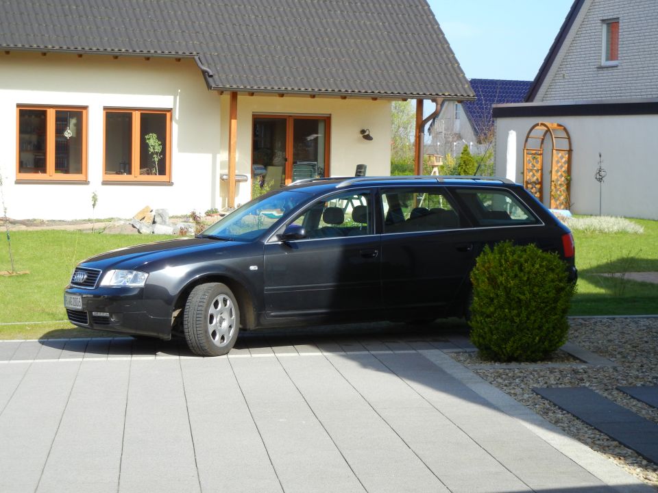 Dark sedan parked on a paved driveway in front of a house
