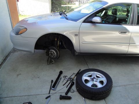2003 Ford Taurus - A silver 2003 Ford Taurus sedan is parked outside with its front passenger wheel removed and tools laid out for repair.