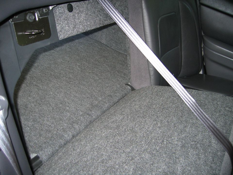 Rear seat floor and carpeted area with seat belt strap across a folded grey upholstered seat