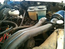 1988 Ford Bronco - The engine bay of a vehicle, an aftermarket air intake system with a blue filter and modified exhaust pipes.