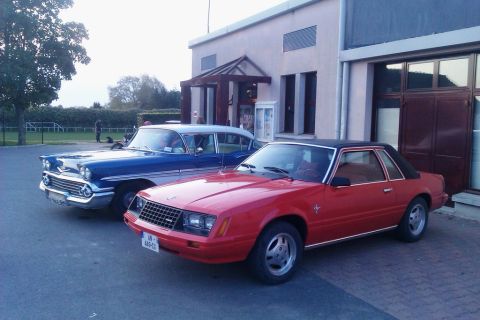 1991 Ford LTD Crown Victoria - Two classic cars, a red Ford Mustang and a blue sedan, are parked outside a building.
