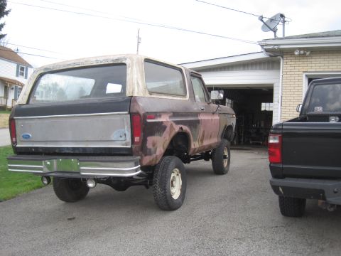 1979 Ford Bronco - This lifted Ford Bronco is parked in a driveway next to a black pickup truck, with a garage in the background.