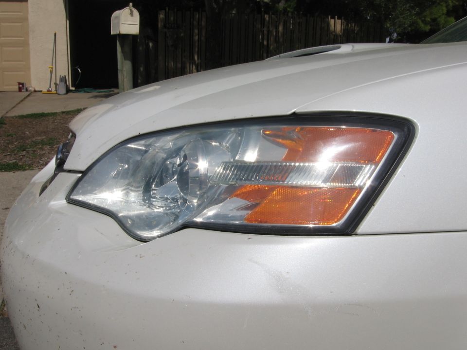 White car front bumper and headlight with orange turn signal. Hood scoop visible