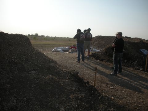 1996 Ford Bronco - Several individuals are gathered in an outdoor area, possibly filming an event, with large piles of dirt and sandbags visible.