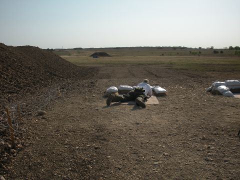 1996 Ford Bronco - A person lies prone behind sandbags in a desolate, open field under a clear sky.