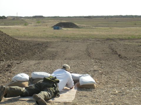 1996 Ford Bronco - A person lies prone behind sandbags at a shooting range, with targets and berms visible in the distance.