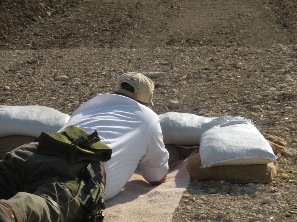 person lying down at a shooting range, using sandbags for support