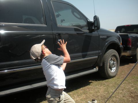 1996 Ford Bronco - A child reaches for the door handle of a black Ford Super Duty truck, with another truck visible in the background.