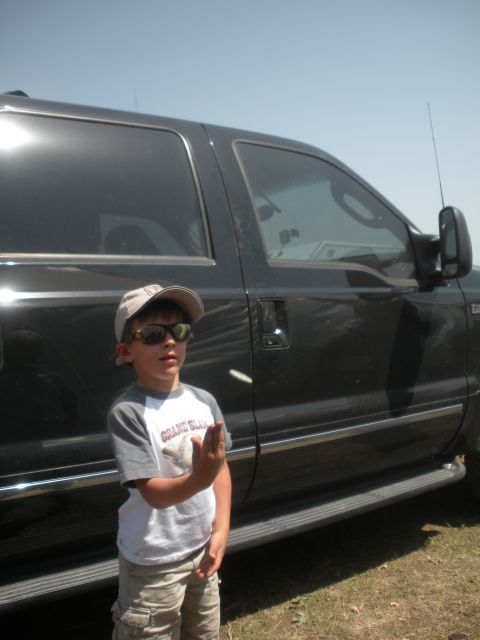 1996 Ford Bronco - A young boy poses next to a large black SUV on a sunny day.