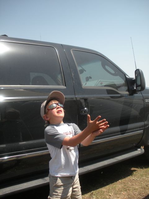 1996 Ford Bronco - A young boy stands next to a large truck, looking up at the sky with his hands outstretched.