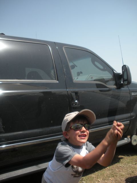 1996 Ford Bronco - A child stands in front of a black SUV, looking up and holding something in their hands.