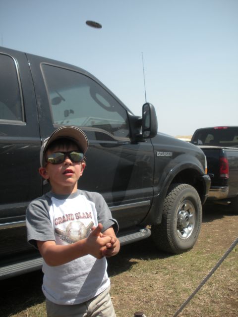 1996 Ford Bronco - A young boy stands in front of a large black truck, with another truck visible in the background under a clear sky.