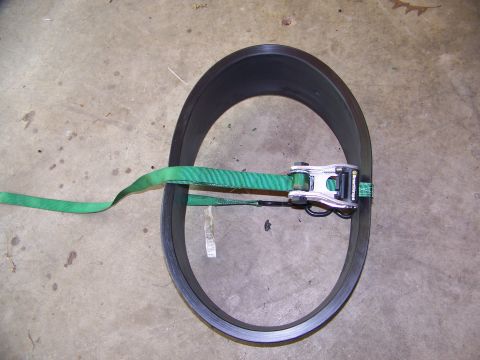 2001 Dodge 1500 - A black ring, possibly a tire or wheel component, is secured with a green ratchet strap and metal buckle on a concrete surface.