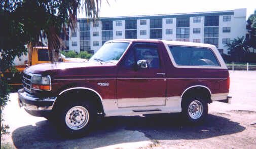 Maroon full-size Bronco with tan lower trim parked in front of a multi-story building