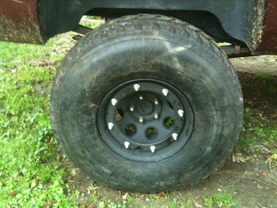 Close-up of a black aftermarket wheel with chrome lug nuts on a large off-road tire