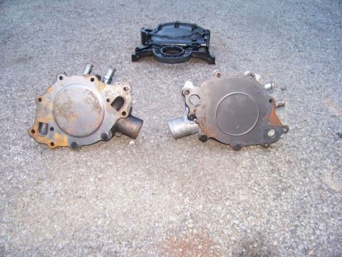 1978 Pontiac Trans Am - Two used water pumps and a timing cover are laid out on a paved surface.